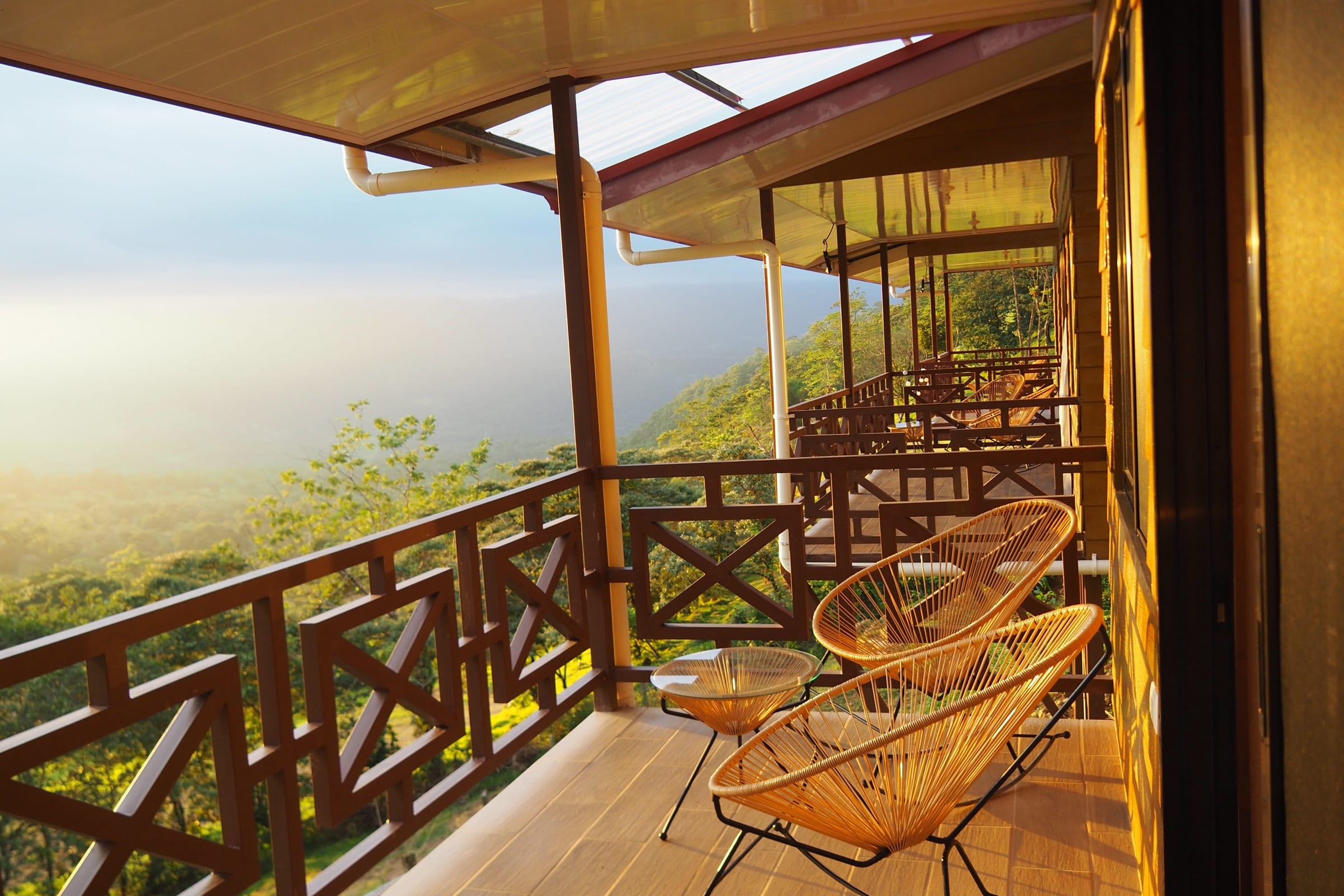 The covered terrace of a bungalow at golden hour, rocking chairs facing the fog filling the valley